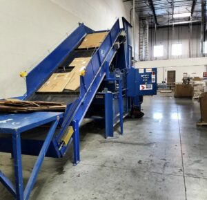 A large industrial cardboard baler and recycling system in operation, managed by Premier Service in North Las Vegas, NV.