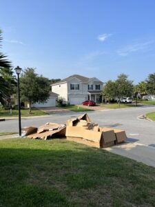 A large pile of flattened cardboard boxes on a residential lawn awaiting removal by Junk Fade Away, LLC in Jacksonville, FL.