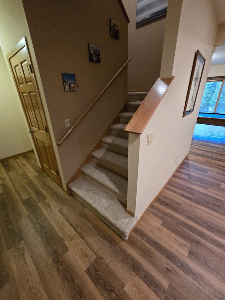 A residential staircase with carpeted steps and new wood-look laminate flooring by L.A. Floors in Madison, WI.