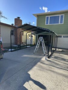 A partially constructed carport frame with a ladder in a driveway, showing a handyman job by B4 It Breaks in Billings, MT.