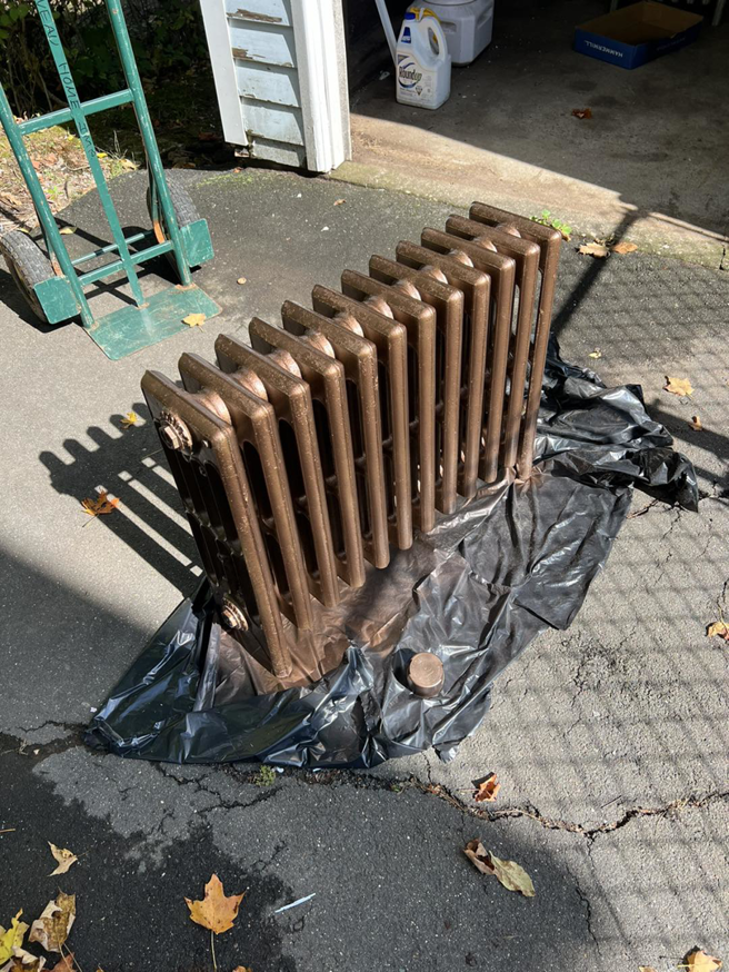 An old cast iron radiator being painted on a tarp, a home improvement service by Corriveau Home Improvement LLC in Bristol, CT.
