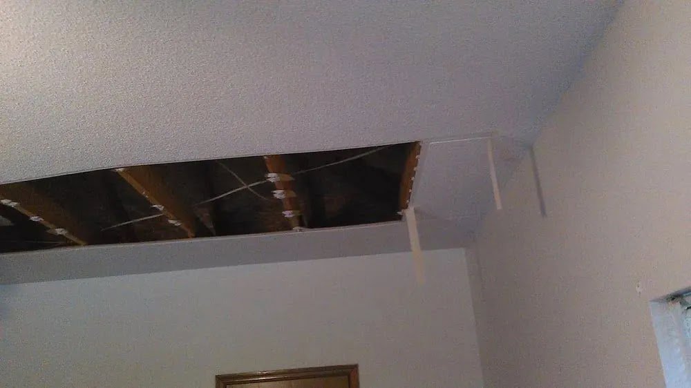 A ceiling with a section of drywall cut out, exposing joists and wiring during a repair by Ceiling Doctor by Julian in Augusta, GA.