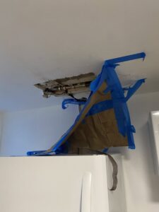 A ceiling leak with exposed pipes and temporary catch, indicating water damage repair by Infinity Handyman in Anchorage, AK
