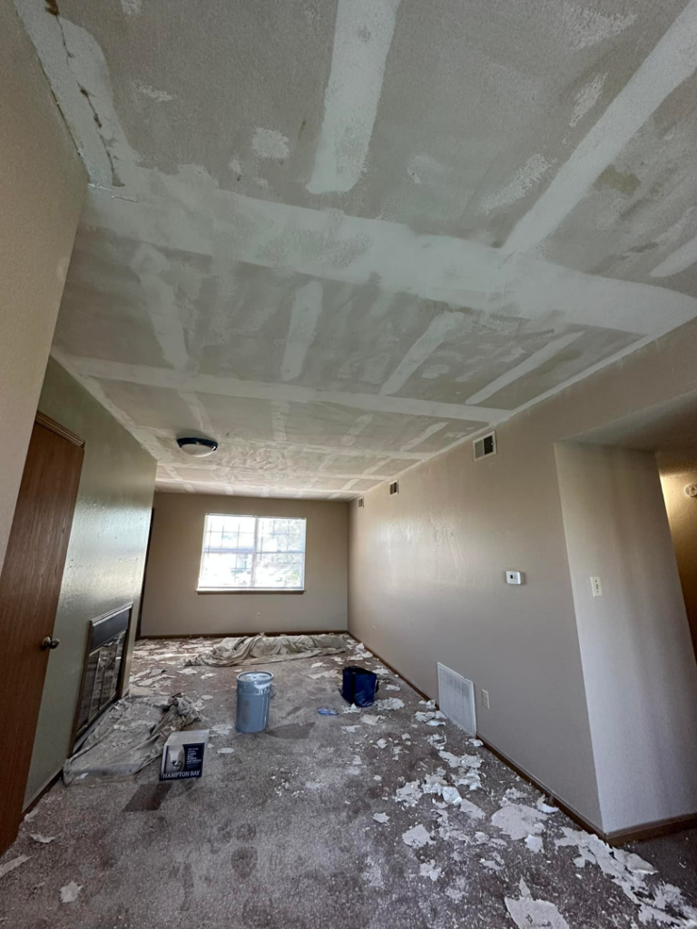 A room undergoing ceiling repair with drywall patching visible and painting supplies on the floor, handled by One Seven Painting LLC in Columbia, MO.
