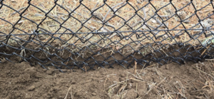 Close-up of a black chain-link fence base secured into the ground by Michel's Fencing in Bend, OR