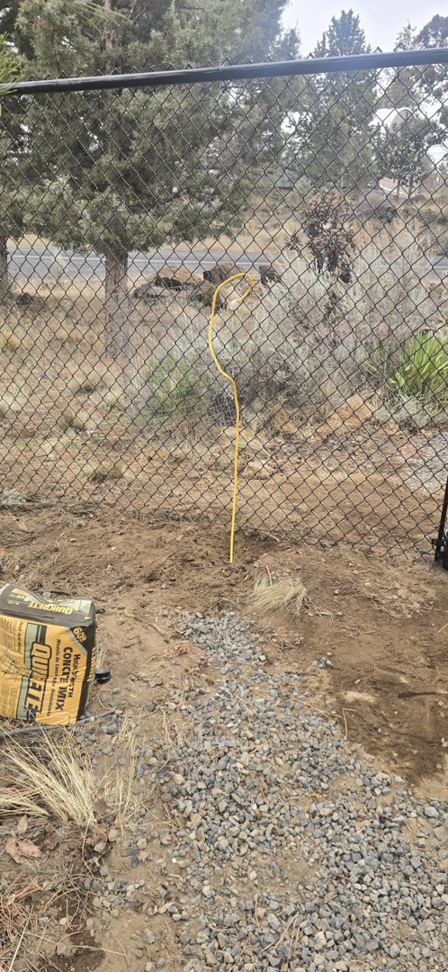 Chain-link fence installation in progress with a bag of concrete mix and gravel by Michel's Fencing in Bend, OR