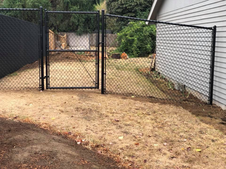 A black chain-link fence with an access gate installed next to a residential building by J & M Fence Co. in Vancouver, WA.