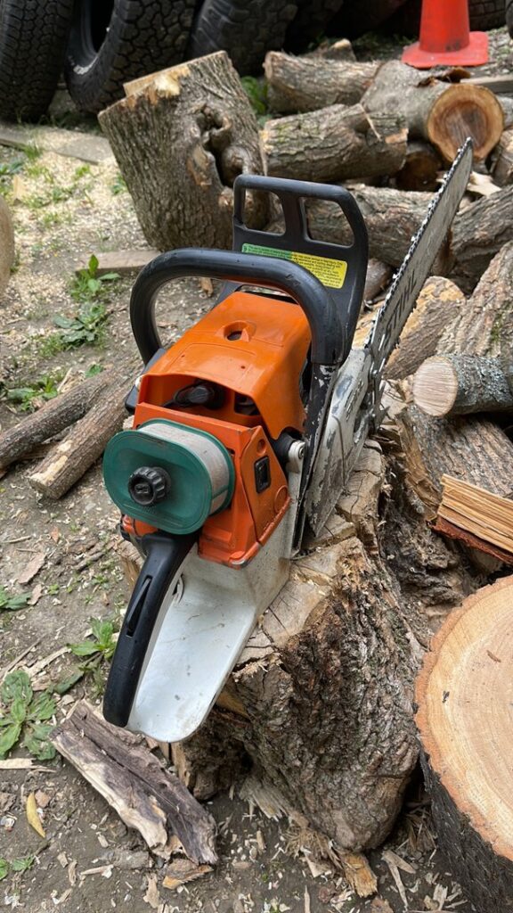 A chainsaw resting on a tree stump with cut logs in the background, representing the equipment used by Russell Tree Works & Firewood Sales in Augusta, ME.