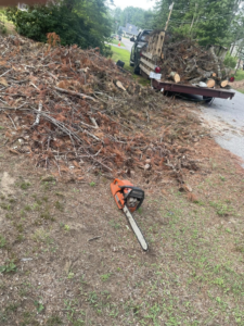 A chainsaw on the ground next to a large pile of yard debris and branches, ready for hauling by Mr. Property Service in Sanford, ME.