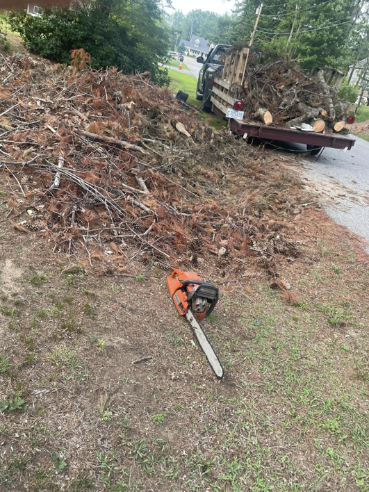 A chainsaw on the ground next to a large pile of yard debris and branches, ready for hauling by Mr. Property Service in Sanford, ME.