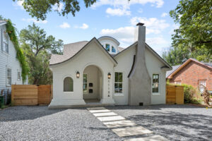 A charming white brick house featuring an arched entryway and a dark roof, showcasing new construction by Stone Acorn Builders in Bellaire, TX.