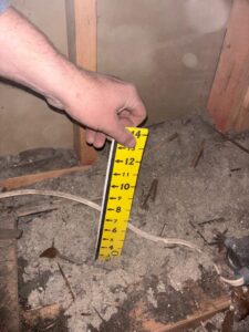A hand holding a ruler to check the level of loose-fill insulation in an attic, a service from Pacific Insulation & Mold Remediation in Spokane, WA.