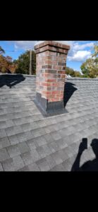 A brick chimney with new flashing on a shingled roof, repaired by Class General Contracting in West Springfield, MA.