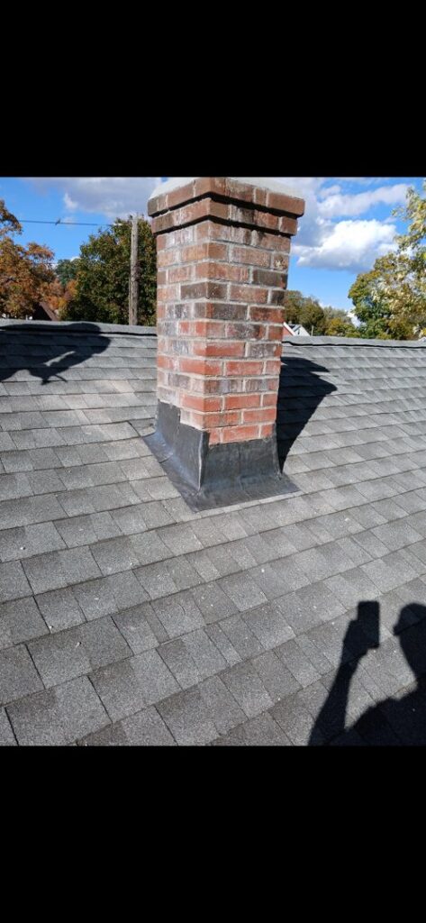 A brick chimney with new flashing on a shingled roof, repaired by Class General Contracting in West Springfield, MA.