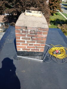 Tools and a brick chimney on a flat roof, ready for repair by Class General Contracting in West Springfield, MA.