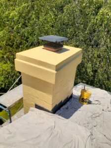 A chimney undergoing repair or sealing, with a bucket of 'Stik' sealant and drop cloths, by Modern Wall Systems in Virginia Beach, VA.