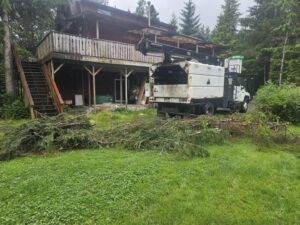 A chipper truck and a pile of cut branches on a residential lawn after tree cleanup by Timberscape Industries LLC in Ketchikan, AK.