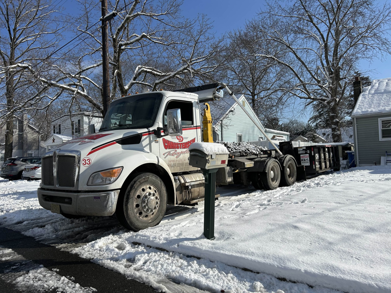 A Christensen Recycling truck delivering a dumpster in a snowy residential area in Sayreville, NJ.