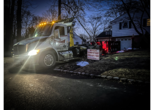 A Christensen Recycling truck picking up a dumpster in a residential area at night in Sayreville, NJ.