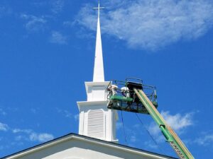 Workers in an aerial lift painting a church steeple, a specialized handyman painting service by Randy Overacre Painting Company in Virginia Beach, VA.