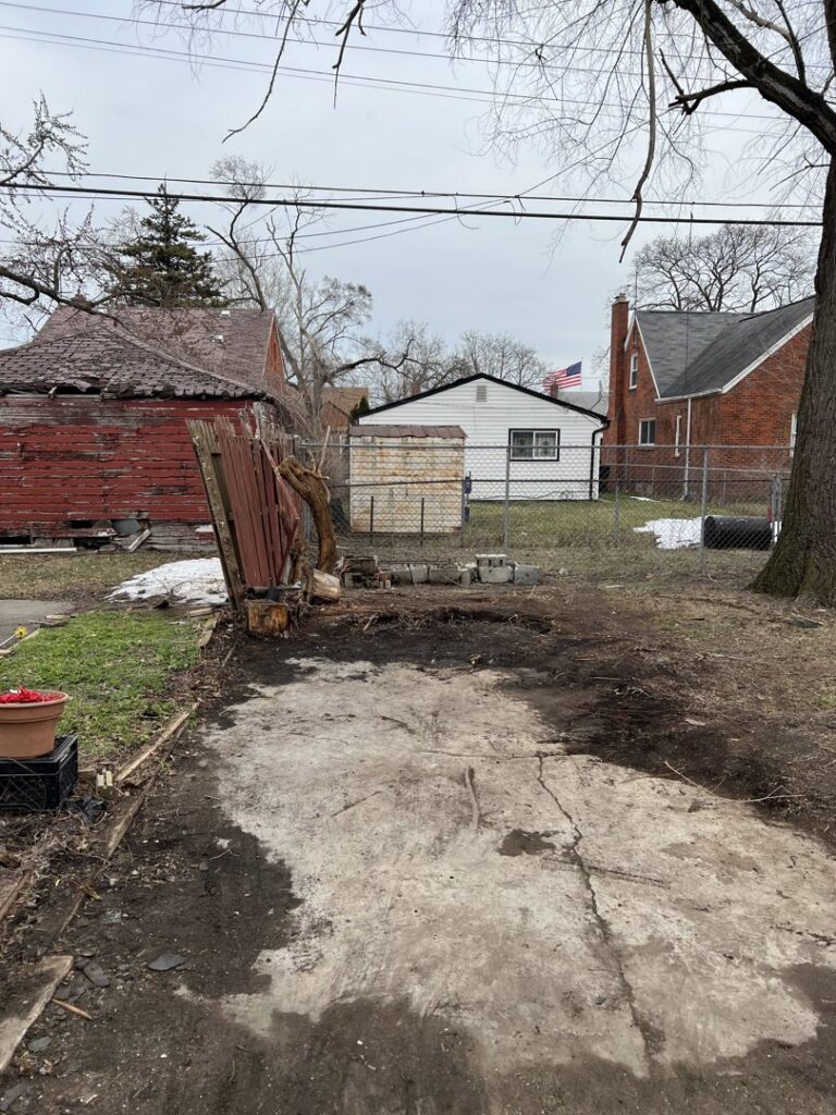 A cleared backyard with a concrete path, showing the result of a demolition or yard waste removal service by Prestige Junk Removal & Hauling in Detroit, MI.