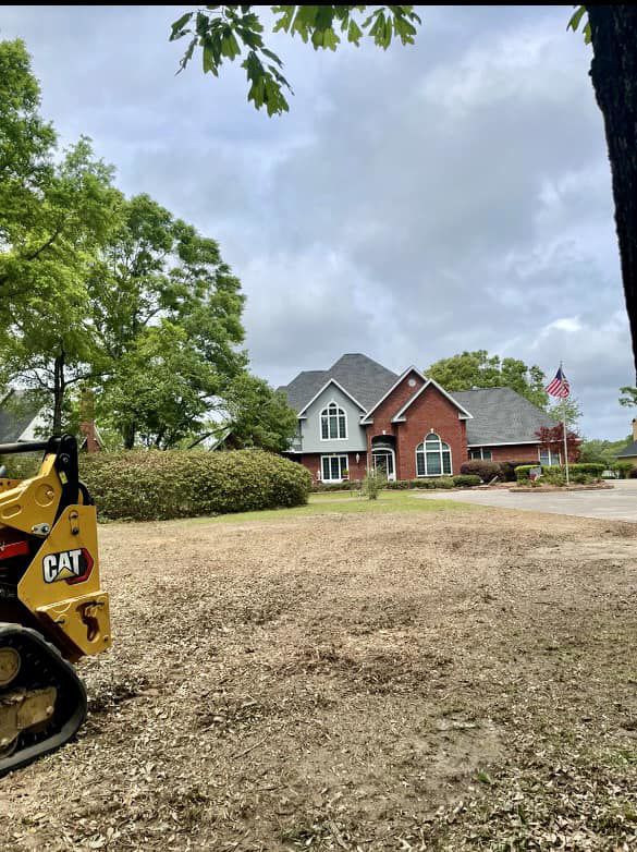 A cleared residential area with a CAT skid steer, showing debris from tree removal by Chappell Tree Service in Mobile, AL.