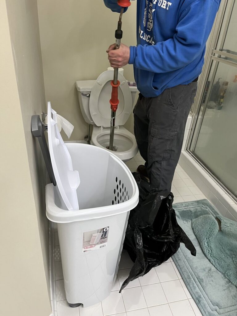 A plumber clearing a clogged toilet with an auger during a service call from JF Plumbing & Heating in Rockville, MD.
