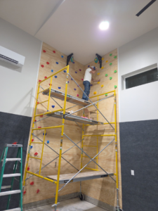 A handyman from SG Service, LLC installing climbing holds on a custom climbing wall in Lincoln, NE