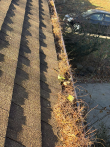 A residential gutter heavily clogged with dry leaves and branches, indicating a need for cleaning by Zamora Roofing & Construction LLC in Madison, WI.