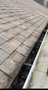 A clogged roof gutter filled with leaves and debris, showing a need for cleaning by Shifting Sands Contracting in Alvordton, OH.