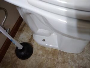 A plunger next to a toilet, indicating a clogged toilet plumbing service by Lincoln Household Services in Lincoln, NE.