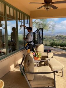 Close-up of a handyman from Bring The Pane cleaning an exterior residential window with a squeegee in Lewiston, ID.