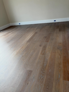 A close-up view of newly installed hardwood floors with white baseboards by Heritage Floors of Hanover LLC in Mechanicsville, VA.
