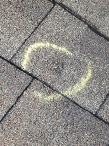 A close-up of a roof shingle with a chalk circle marking hail damage by RRC Reign Roofing & Construction in Oklahoma City, OK.