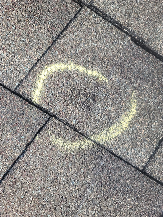 A close-up of a roof shingle with a chalk circle marking hail damage by RRC Reign Roofing & Construction in Oklahoma City, OK.
