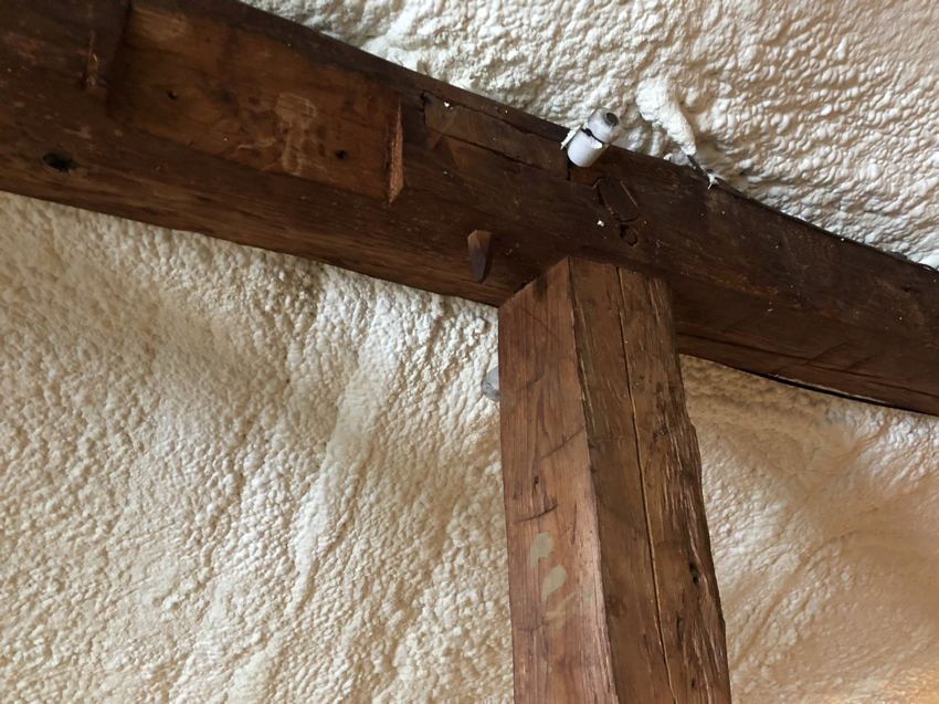 Close-up view of spray foam insulation applied to a wall and wooden beam by Safco Foam Insulation in Hampden, MA.