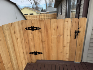 A close-up view of a wooden privacy fence gate with decorative black hinges and a latch, installed by Bergmann Fencing Co. in Cedar Falls, IA.