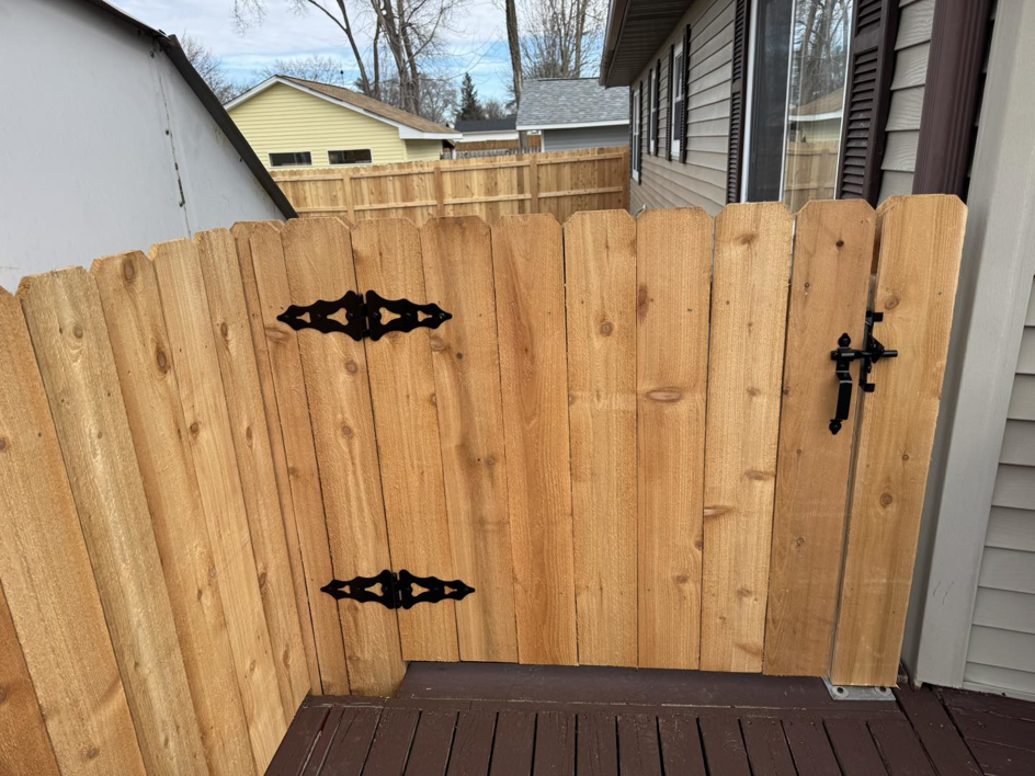 A close-up view of a wooden privacy fence gate with decorative black hinges and a latch, installed by Bergmann Fencing Co. in Cedar Falls, IA.