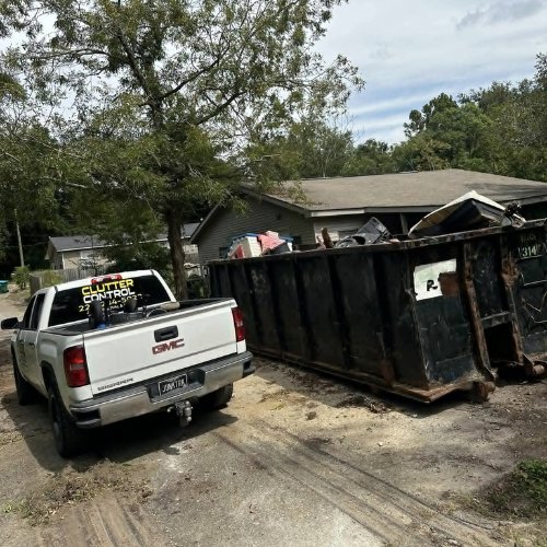 A Clutter Control Junk Removal and Demo truck parked next to a large, full dumpster at a job site in Biloxi, MS.
