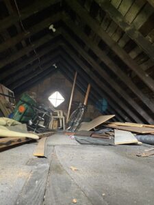 A cluttered attic filled with old furniture, a bicycle, and various debris, ready for junk removal by Sos Junk Removal in Akron, OH.