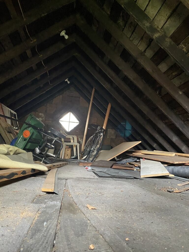 A cluttered attic filled with old furniture, a bicycle, and various debris, ready for junk removal by Sos Junk Removal in Akron, OH.