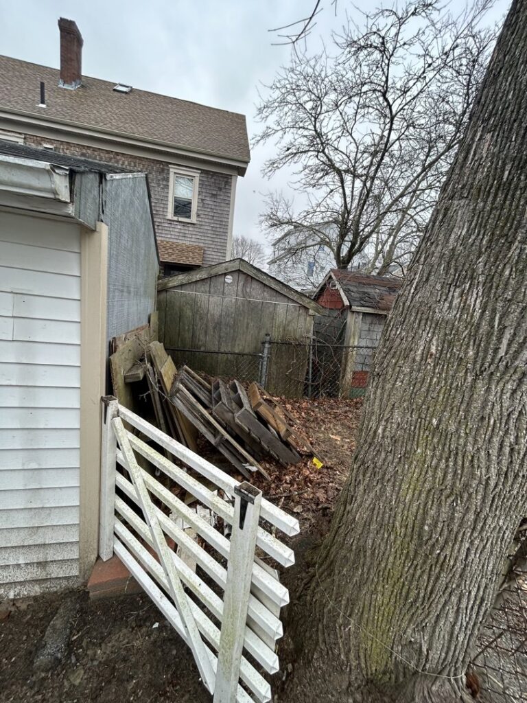 A cluttered backyard with old wood, debris, and a shed, awaiting junk removal by CK Junk Removal in New Bedford, MA
