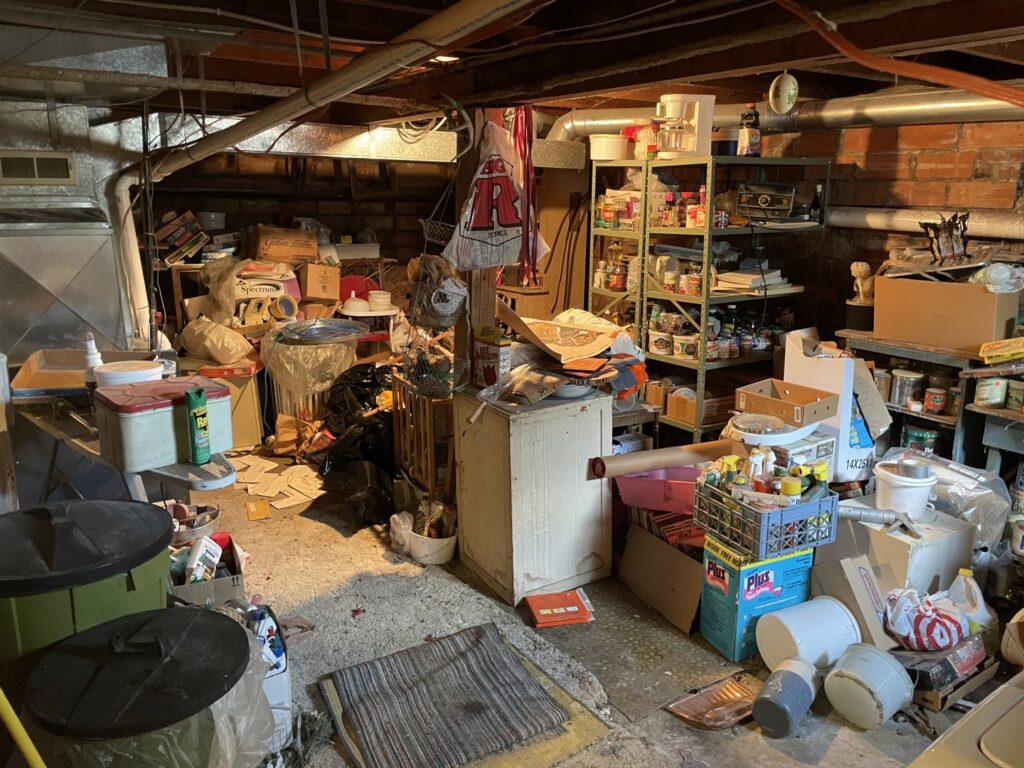 A heavily cluttered basement filled with boxes, old furniture, and various items, ready for cleanout by Hudson's Trash Removal, LLC in Great Falls, MT.