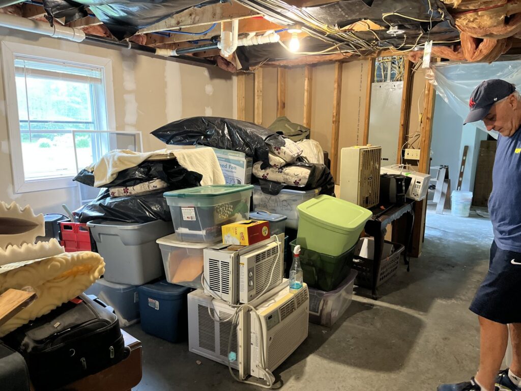 A cluttered basement room filled with boxes, bags, and old appliances, awaiting junk removal by Mr. Property Service in Sanford, ME.