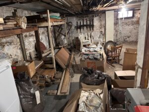 A cluttered basement filled with boxes, old furniture, and various items, ready for junk removal by The Junkluggers in Hicksville, NY.