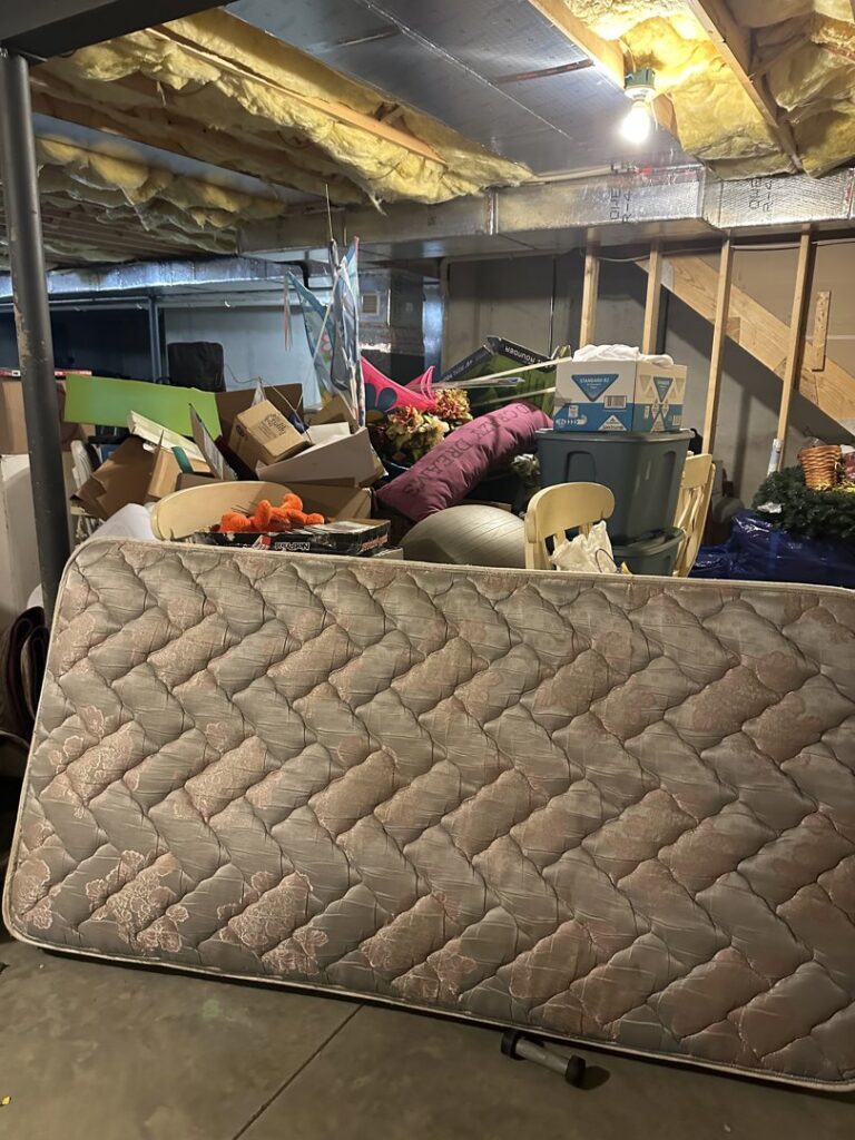 A heavily cluttered basement with a mattress, boxes, and various items awaiting junk removal by Vatter Hauling Service in Lancaster, PA.