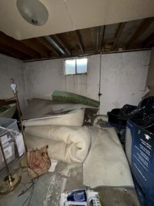 A cluttered basement room with rolled-up carpet, old furniture, and various items, awaiting junk removal by Goblins Junk Removal in Wheat Ridge, CO.