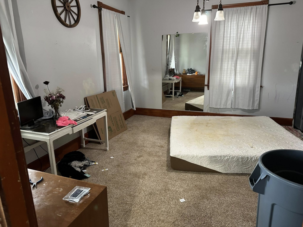 A cluttered bedroom with a mattress on the floor, desk, and boxes, showing a space needing junk removal by Sinclair Waste Removal & Hauling LLC in St. Charles, MO.