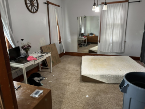 A cluttered bedroom with a mattress on the floor, desk, and boxes, showing a space needing junk removal by Sinclair Waste Removal & Hauling LLC in St. Charles, MO.