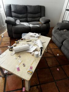 A coffee table and sofa covered in trash and clutter, indicating a junk removal service needed by Affinity Bio Solutions in Phoenix, AZ.